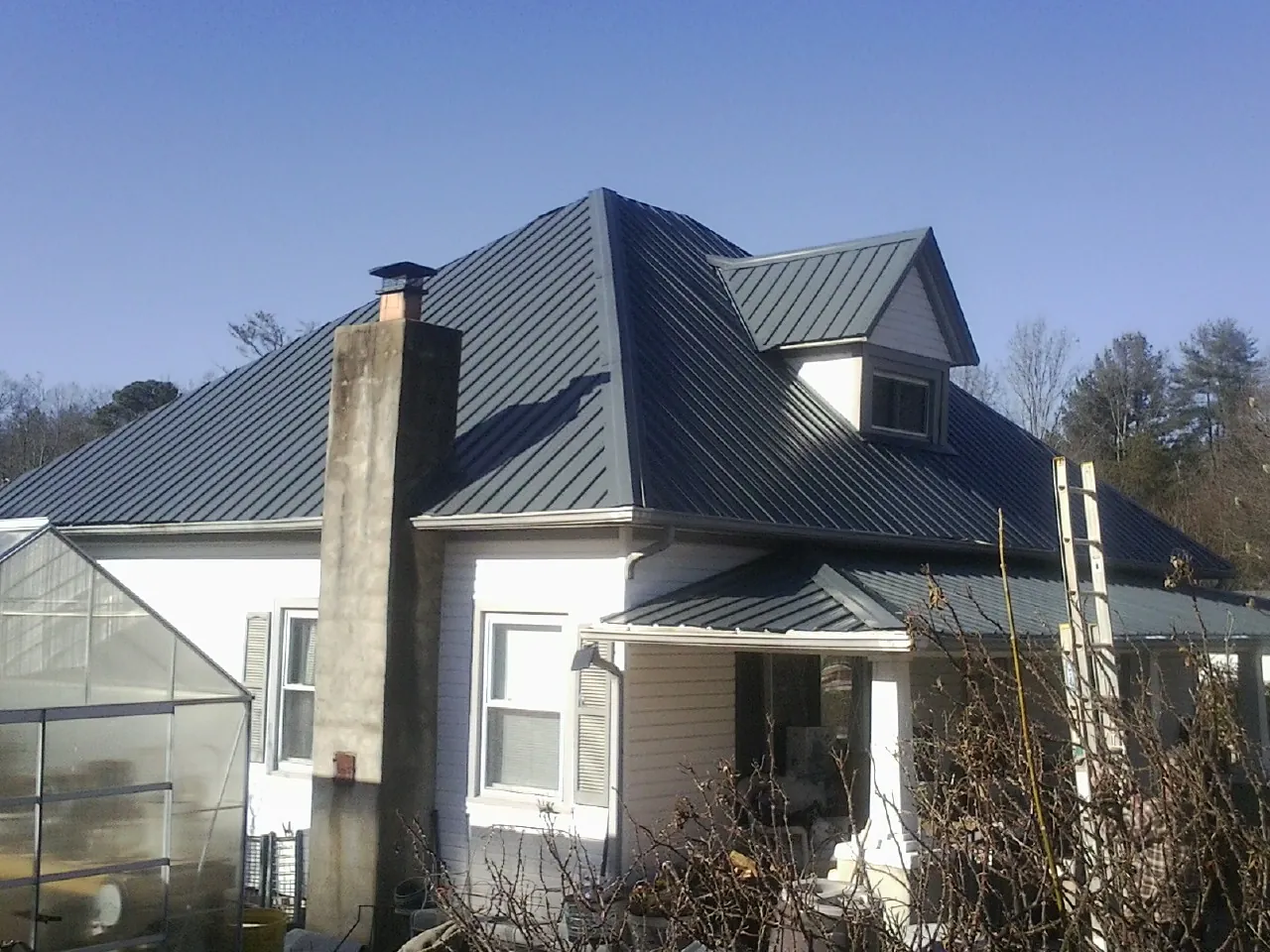 Dark blue standing seam metal roof on a white farmhouse with dormer — Slate & Tile Roof Repair by Roofing Brothers in Brave