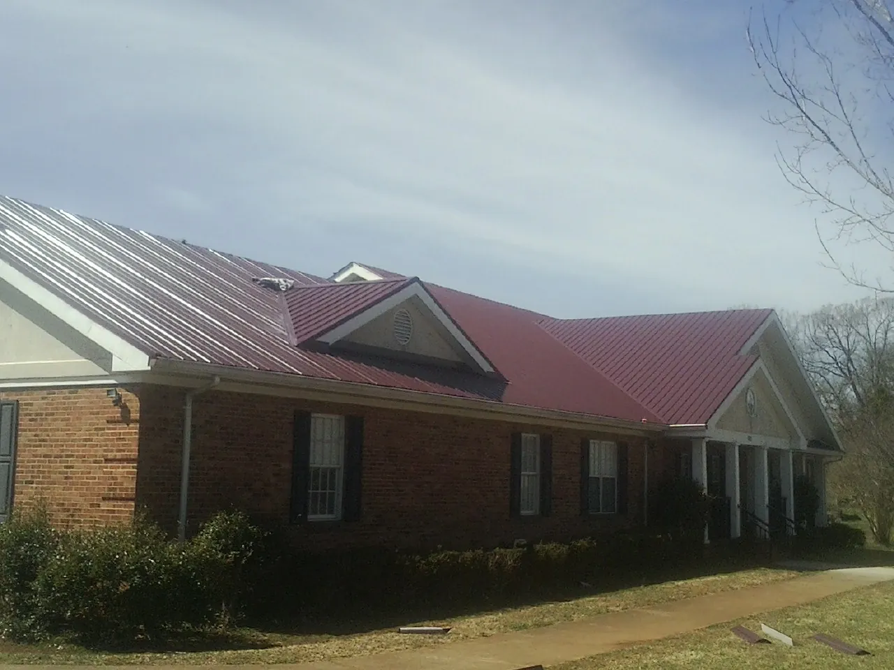 Red metal roof with gabled entries on a long brick building, from a Hail Damage Roof Repair job in Brave