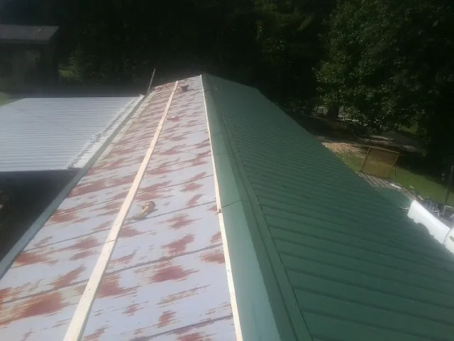Old rusted panels beside newly installed green metal roofing — Wind Damage Roof Repair by Roofing Brothers in Brave