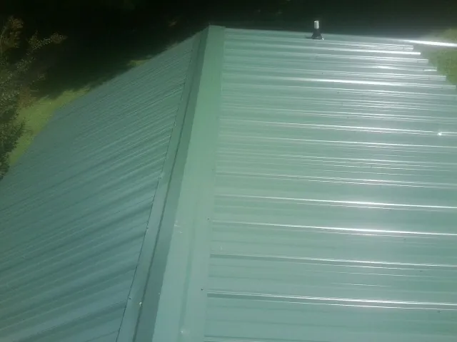 New green metal panels meeting at the ridge of a roof — Flat Roof Repair work by our crew in Brave