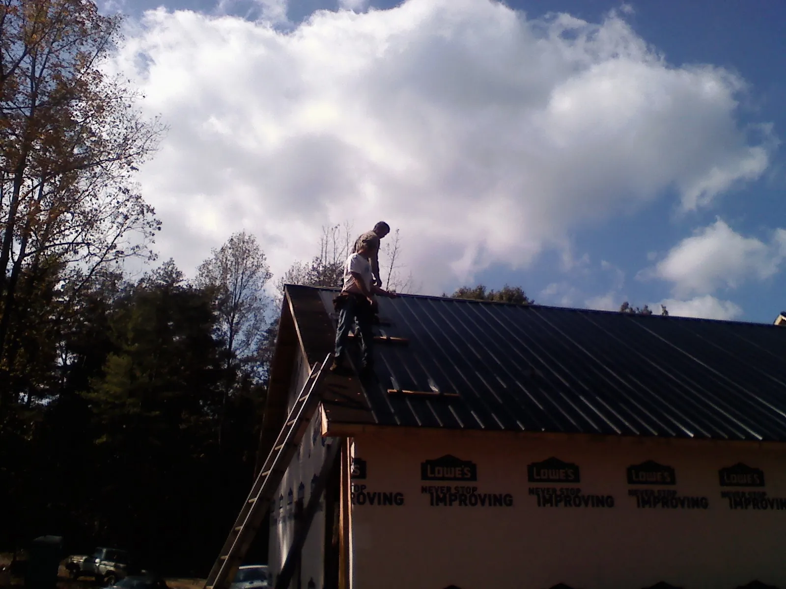 Roofer fastening dark metal panels high against a cloudy sky, from a Roof Inspection job in Brave
