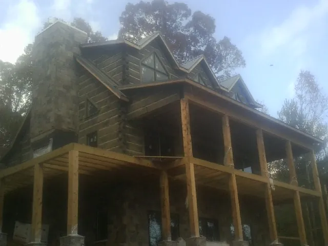 Stone chimney and dormers on a large log home with a timber porch in Brave