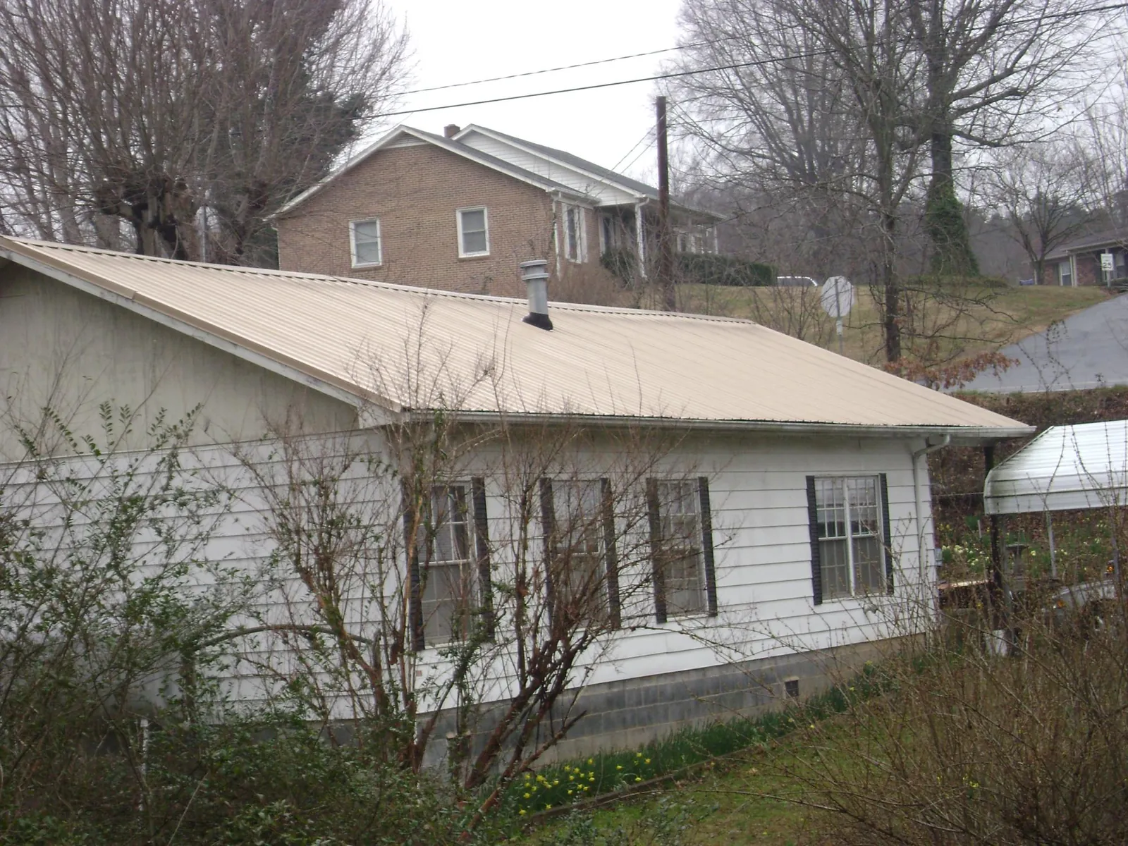 Tan metal roof on a white sided house set into a hillside — Commercial Roofing by Roofing Brothers in Brave