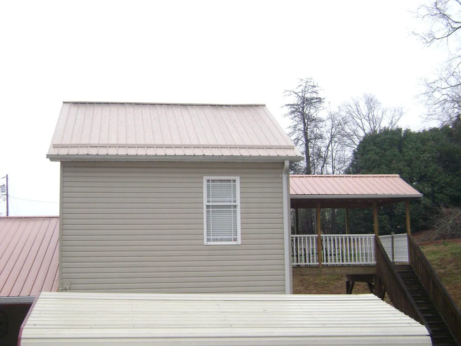 Tan metal roofs on a two story addition and attached porch, from a Roof Replacement job in Brave